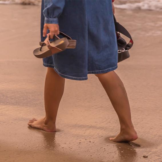 Woman walking on beach with sandals in hand