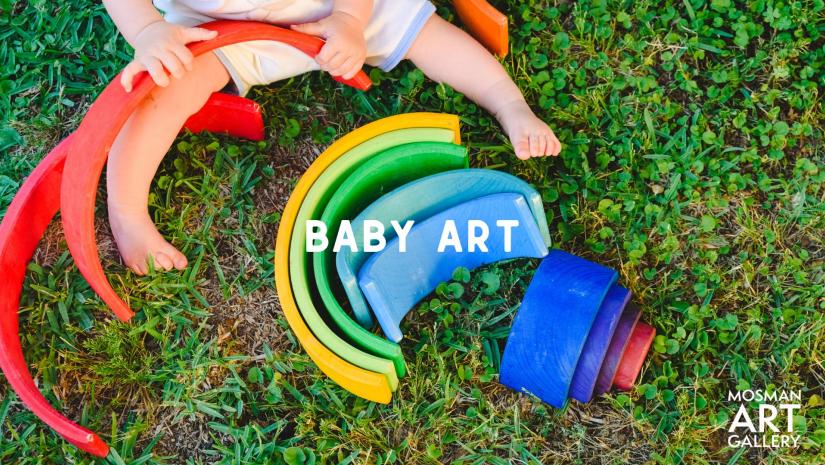 A baby on grass playing with a colourful wooden rainbow