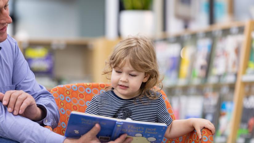 little girl sitting on an orange chair reading a blue picture book