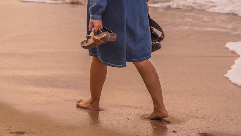 Woman walking on beach with sandals in hand