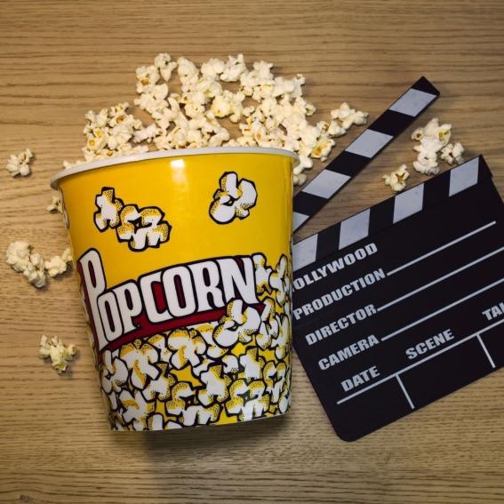 A bucket of popcorn and a movie clipping sign on a wooden table