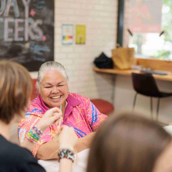 A local aunty smiling at some young people weaving baskets