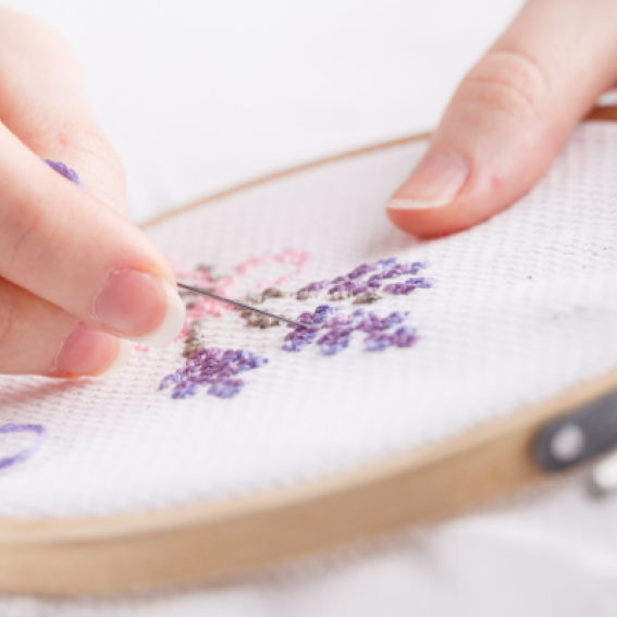 Some purple flowers being cross stitched onto some cloth