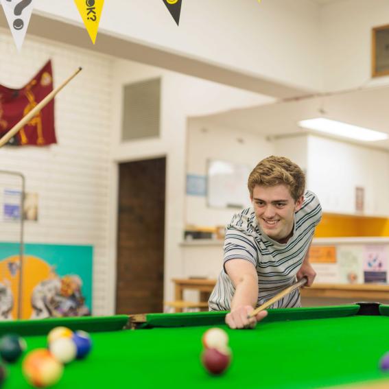 Young person playing pool on a green topped pool table