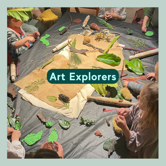 A table with leaves, paper, pencils, clay and organic materials. Children sit around this table, playing and creating artwork.