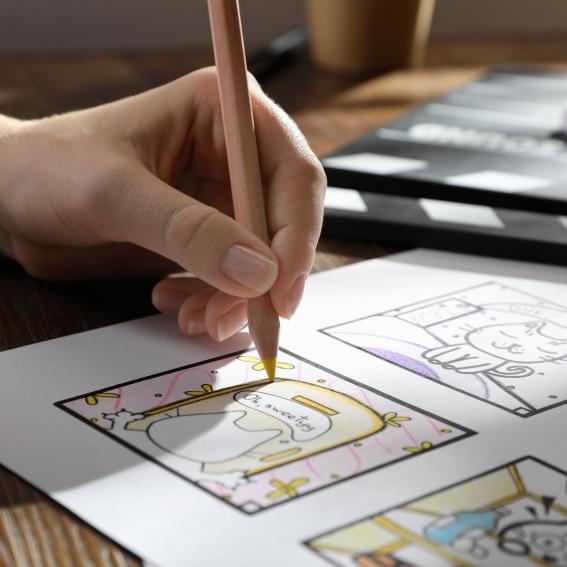Young girl drawing cartoons on paper using a coloured pencil.
