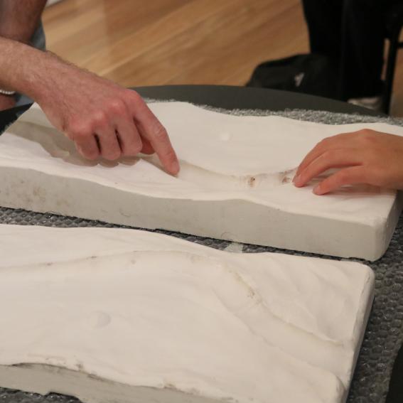 Hands reaching out to touch a clay casting of an artwork