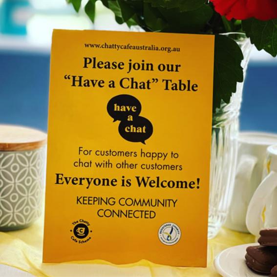 Yellow sign on a table saying "Please join our 'Have a Chat' Table"