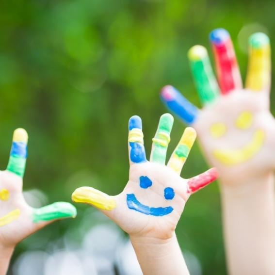 Child's right hand with palm open.  Blue smiley face painted on the palm and each finger painted a variety of colours.