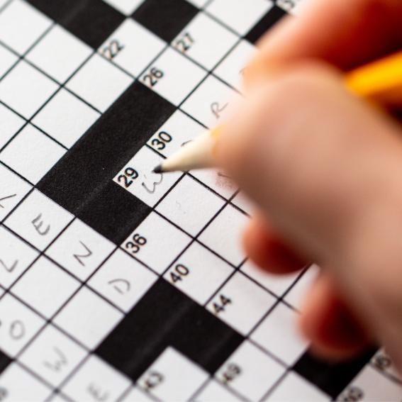 Person completing a black and white crossword with a yellow pencil.