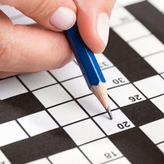 Person filling out a crossword with a blue pencil.
