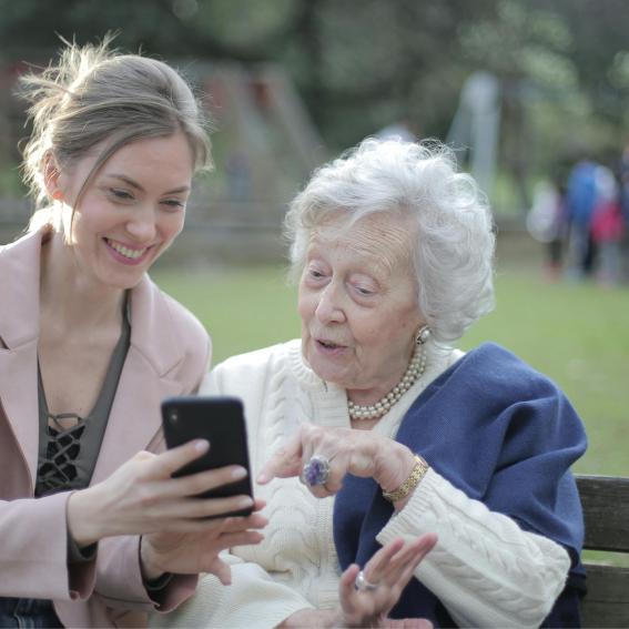 An elderly woman and younger woman sitting on a bench outside.