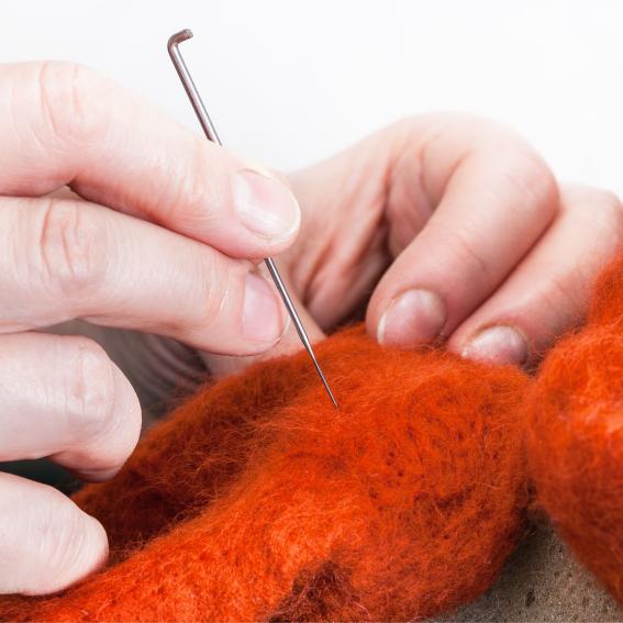A person felting with a needle into orange wool.