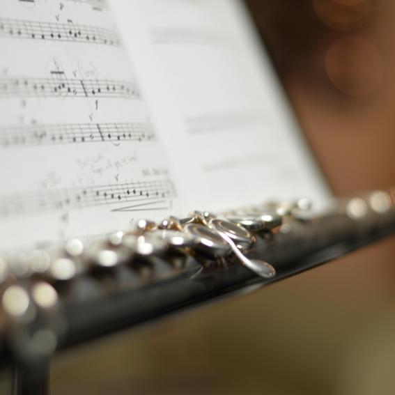 A flute rests in front of sheet music on a music stand.