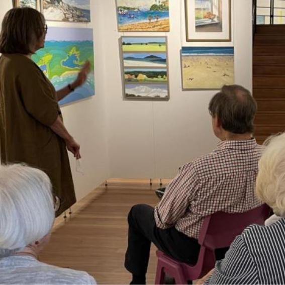 People sitting infront of an artwork as a tour guide describes it