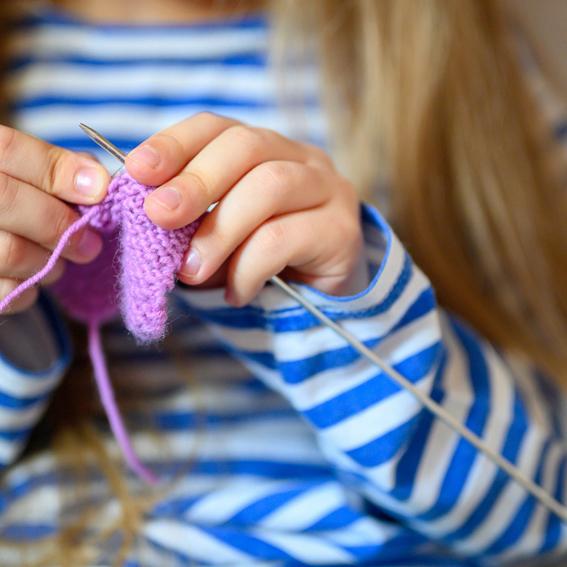 Young girl knitting with purple yarn.