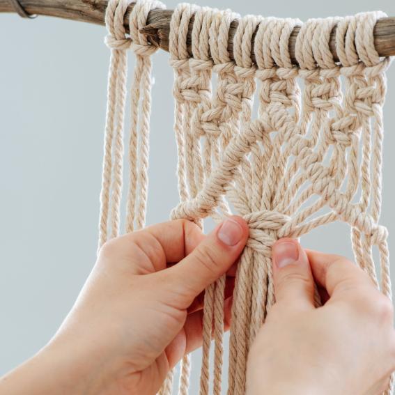 Someone knotting a white macrame hanging.