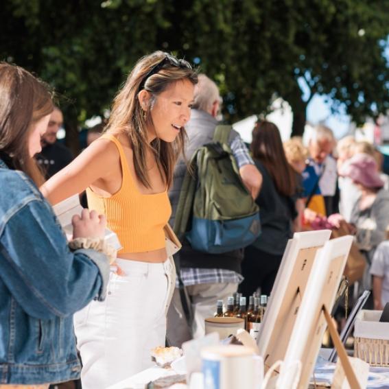 women looking at a market stall and interacting with stall vendor