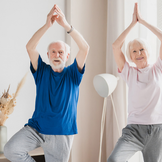 2 Seniors  standing on one leg with the other foot on the inner thigh, in a Tree Pose