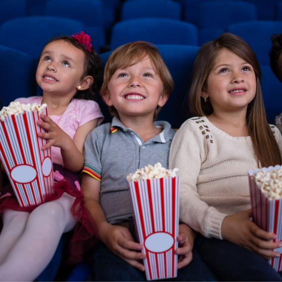 Kids in a row watching a movie holding popcorn.