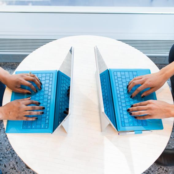 Two blue laptops on a table, two sets of hands typing 