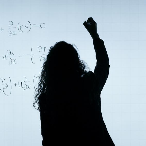 woman with back to camera standing at whiteboard writing numbers