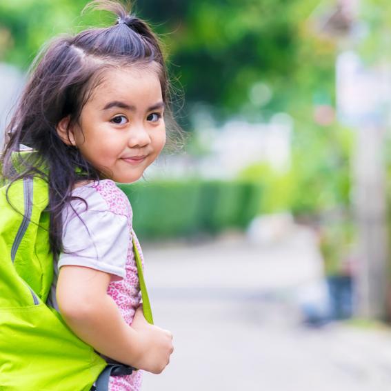 Young girl with a green backpack heading off to school.