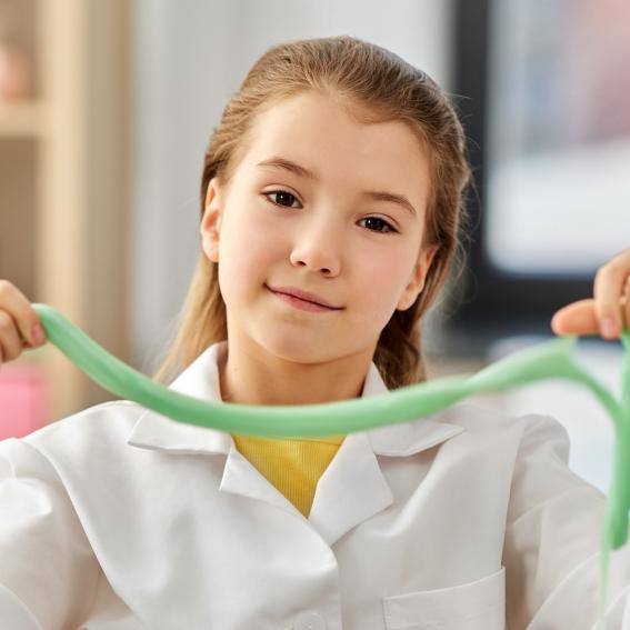 A young girl in a lab coat holding up green slime.