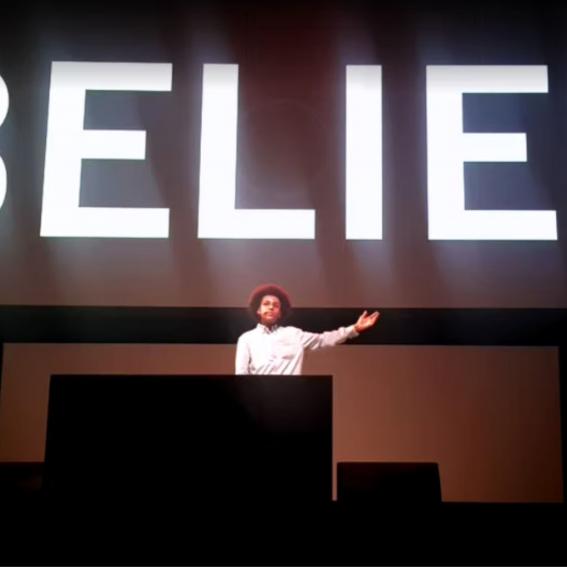 Solli Raphael speaking under a sign saying 'BELIEF'