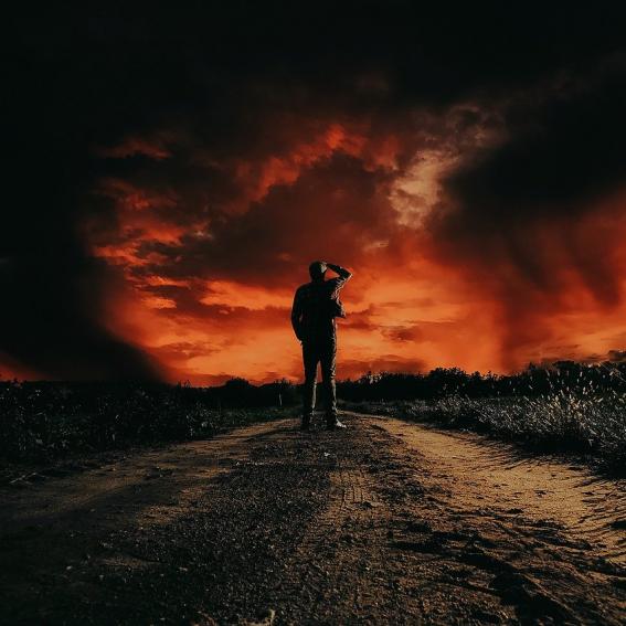 A young person standing in the middle of frame. Surrounded by an ominous dark scene of clouds and colours around them.