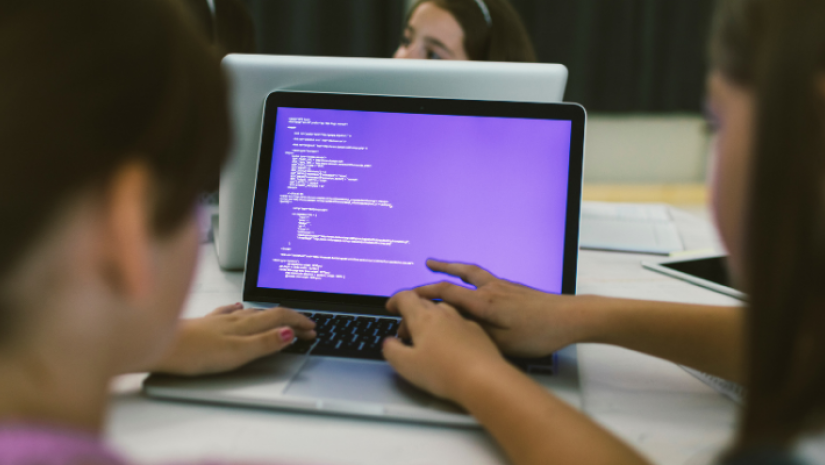 A laptop showing a purple coding screen on a white table