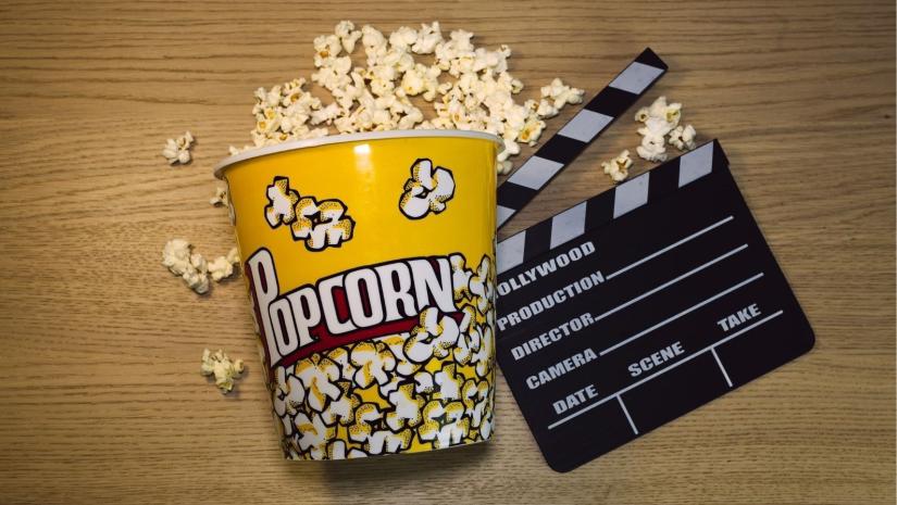 A bucket of popcorn and a movie clipping sign on a wooden table