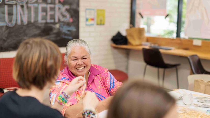 A local aunty smiling at some young people weaving baskets