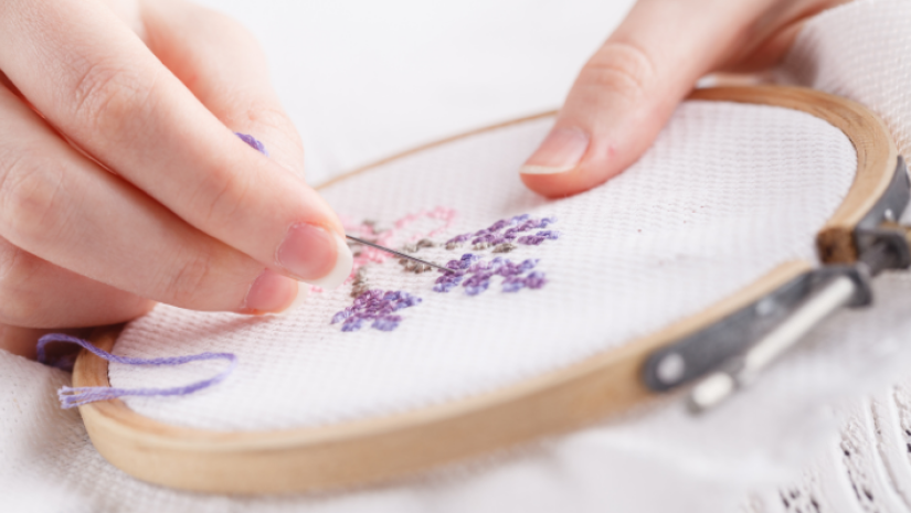 Some purple flowers being cross stitched onto some cloth