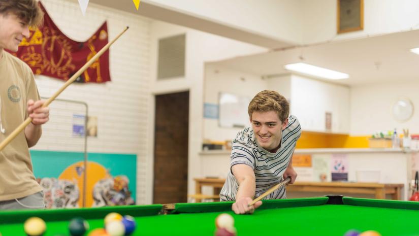 Young person playing pool on a green topped pool table
