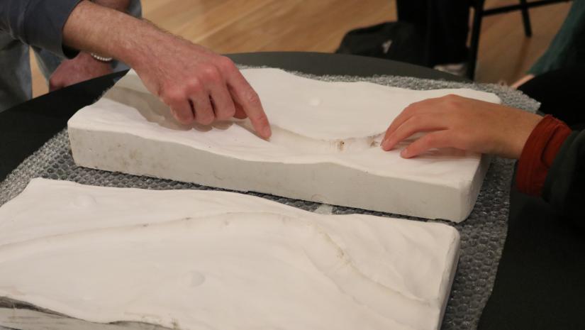 Hands reaching out to touch a clay casting of an artwork