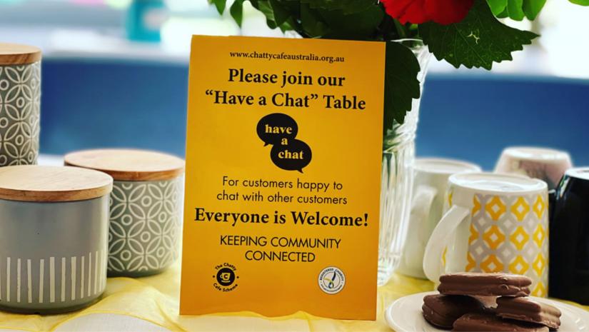 Yellow sign on a table saying "Please join our 'Have a Chat' Table"