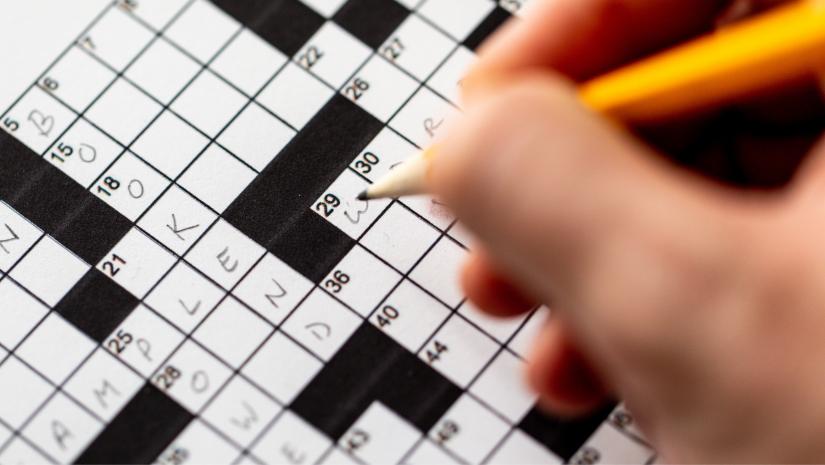 Person completing a black and white crossword with a yellow pencil.