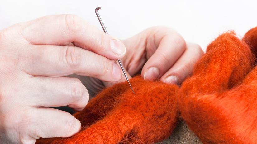 A person felting with a needle into orange wool.