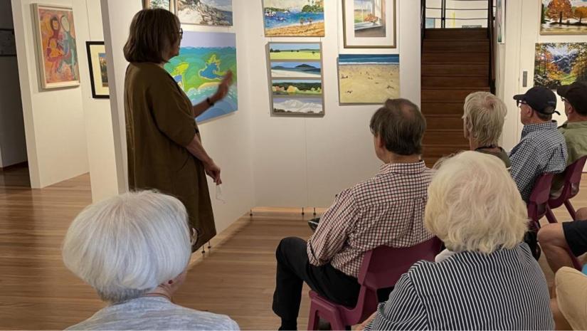 People sitting infront of an artwork as a tour guide describes it