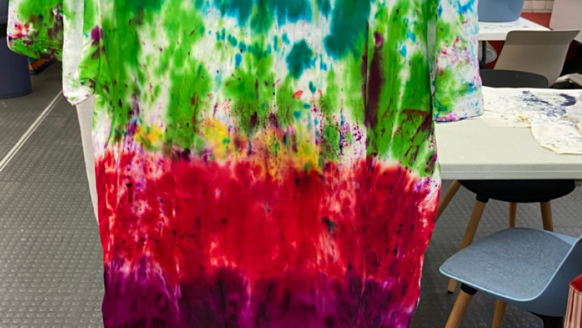 A Tie Dye shirt being held up by a young person in gloves