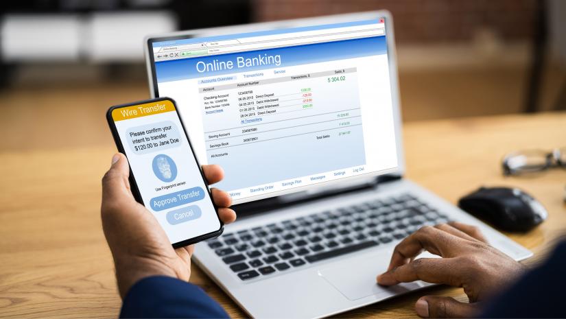 A person using their phone and laptop to access online banking.