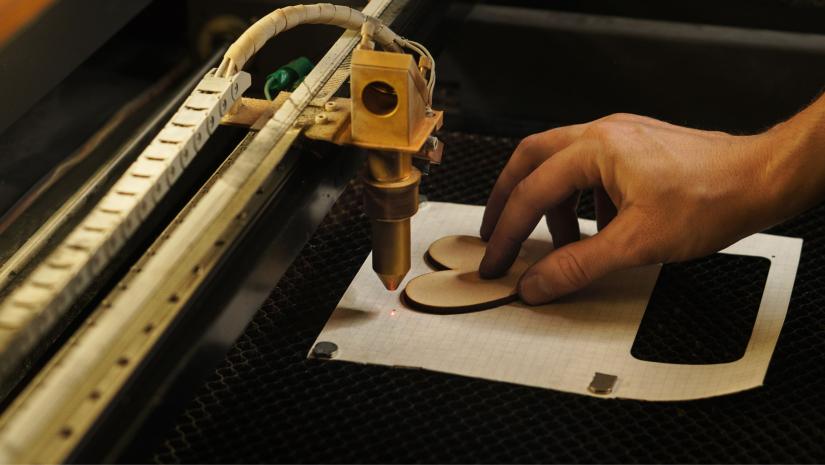 A person using a laser cutter to cut a wooden heart.