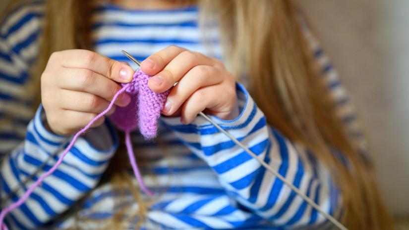 Young girl knitting with purple yarn.