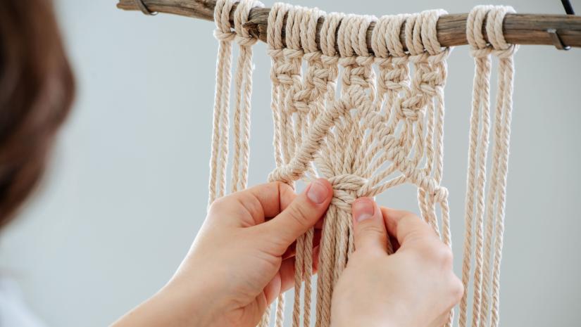 Someone knotting a white macrame hanging.