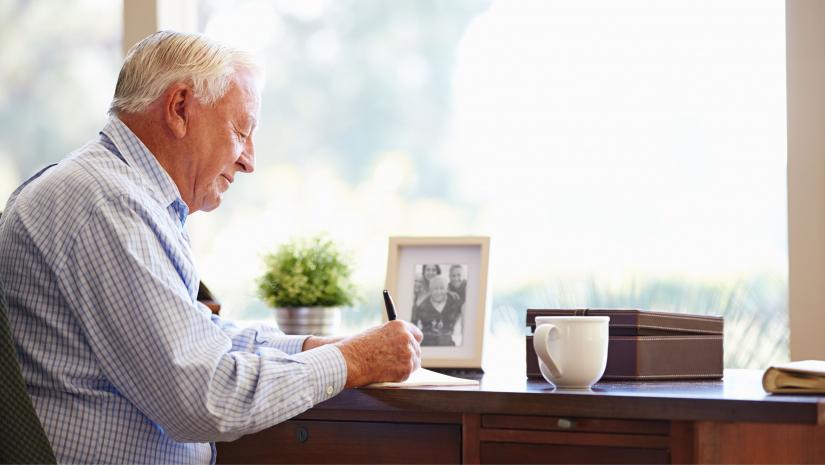 Older gentleman writing in his office.