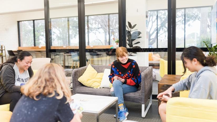 4 young people playing card game on couch