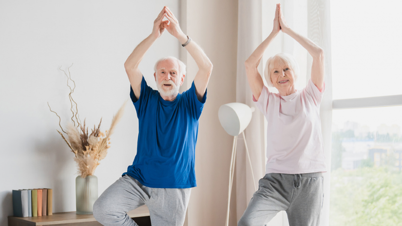 2 Seniors  standing on one leg with the other foot on the inner thigh, in a Tree Pose