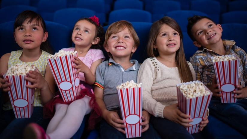 Kids in a row watching a movie holding popcorn.