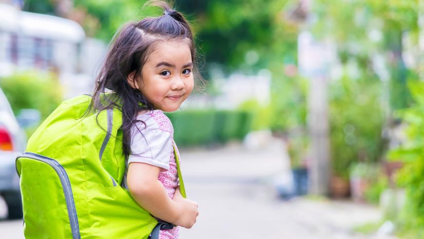 Young girl with a green backpack heading off to school.